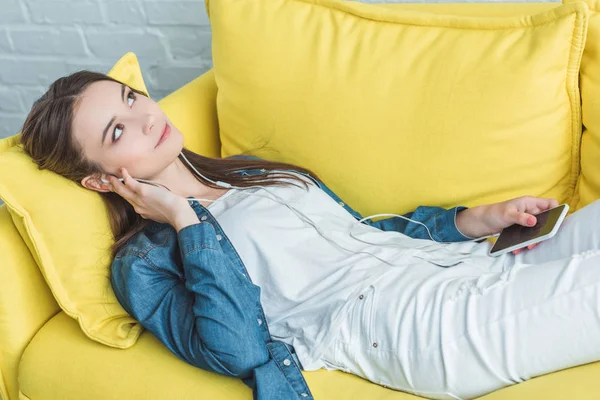 Pensive Smiling Girl Holding Smartphone Listening Music Earphones While Lying — Stock Photo, Image