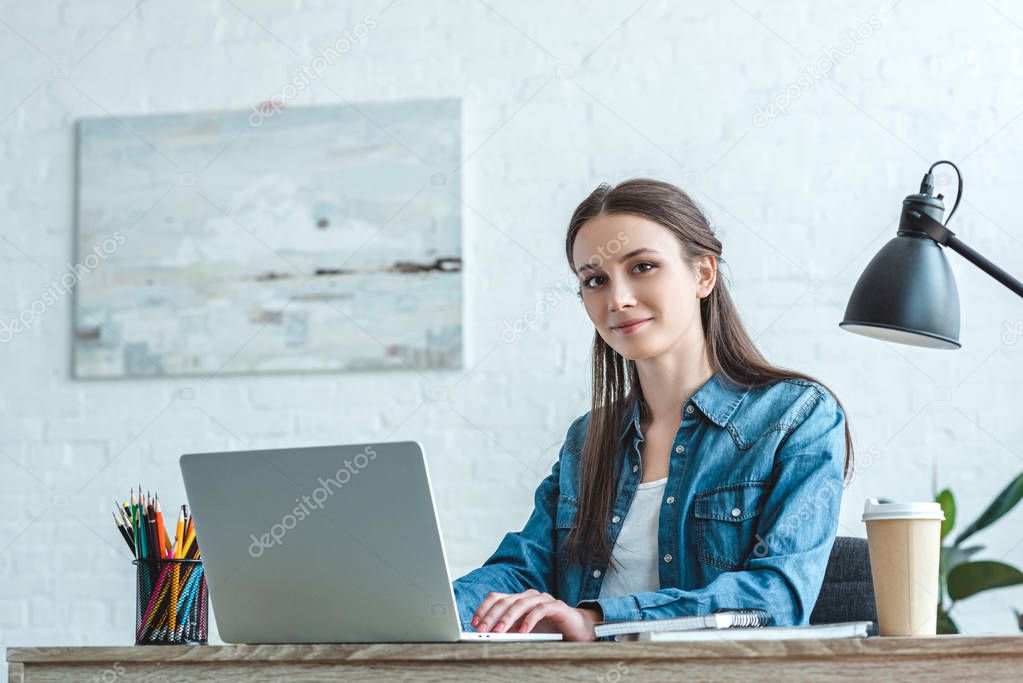 attractive girl smiling at camera while using laptop at desk