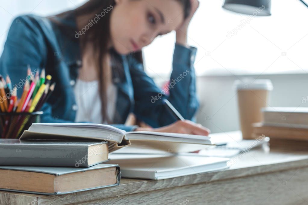 close-up view of books on desk and girl taking notes behind