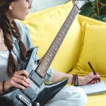 Atractiva chica adolescente tocando la guitarra eléctrica y escribiendo canción