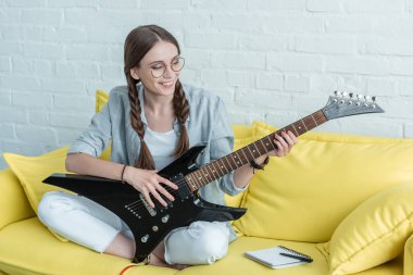 ders kitabı ile sarı kanepede otururken elektro gitar çalmak gülümseyen genç kız 