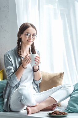 kahve tutarak ve Çerezler ile pencere üzerinde oturan güzel gülümseyen kız