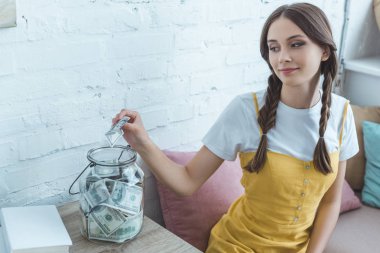 güzel genç kız doları banknot cam kavanoz tasarruf içine koyarak