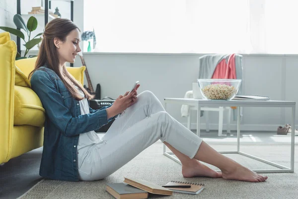 Oldalnézet Használ Smartphone Szőnyeg Könyvek Otthon Ülve Mosolyogva Tizenéves Lány — Stock Fotó