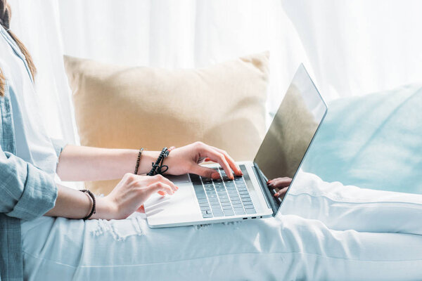 cropped view of woman using laptop while sitting with pillows