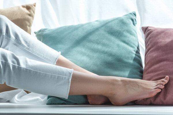 partial view of barefoot female legs near pillows