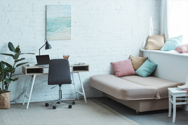 диван с подушками и стол с ноутбуком в гостиной
