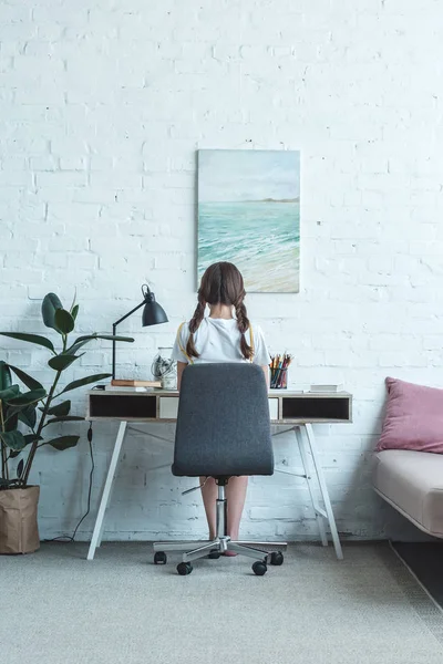 Visão Traseira Menina Sentada Mesa Quarto Com Pintura Parede — Fotografia de Stock