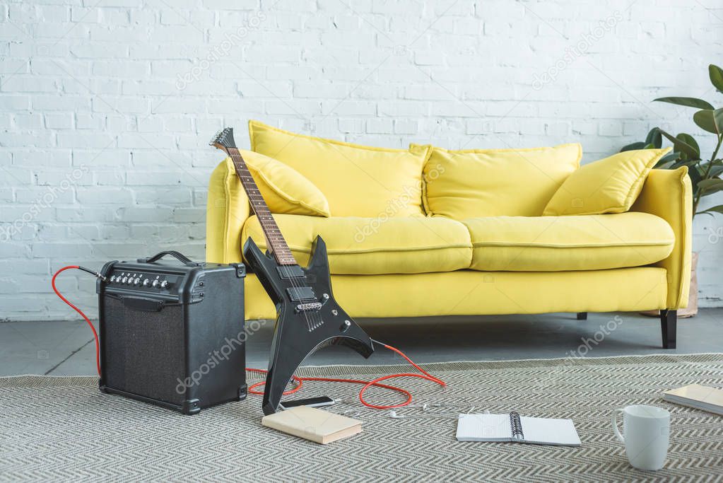 electric guitar, loud speaker, smartphone, books and cup of coffee on floor near yellow sofa in living room