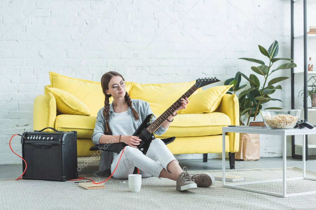 female teen musician playing electric guitar on floor in living room