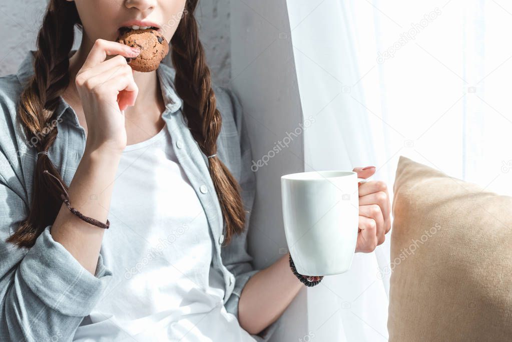 cropped view of girl eating cookie and drinking coffee