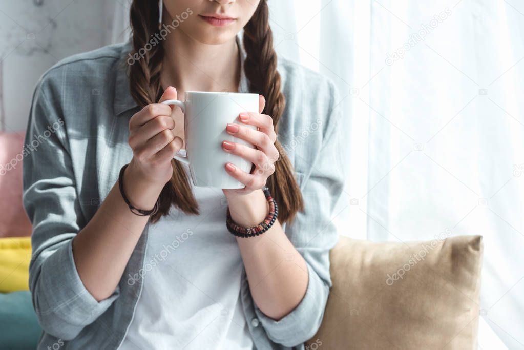 cropped view of teen girl with cup of coffee