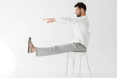 keten giysiler uzanmış bacakları ve eller ile sandalye üzerinde oturan erkek model yan görünümü gri arka plan üzerinde izole 