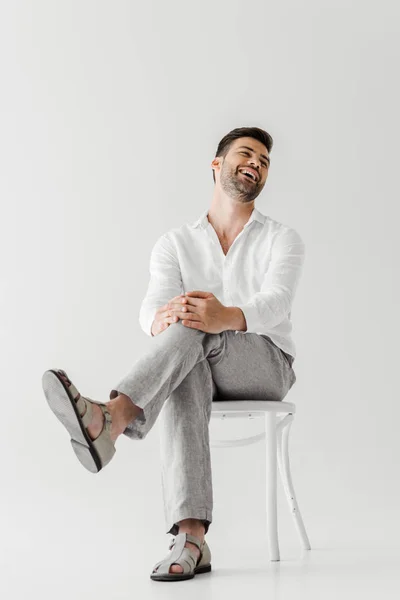 laughing man in linen clothes sitting on chair isolated on grey background