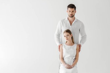 sevgilisini arkasında izole üzerinde gri arka plan ayakta iken sandalye üzerinde oturan keten beyaz elbiseli güzel kadın 
