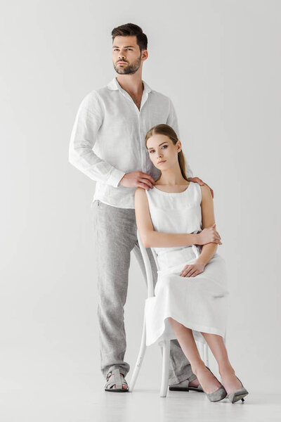 Красивый мужчина обнимает девушку в льняном белом платье сидя на стуле изолированы на сером фоне
