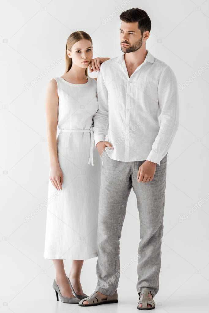 young woman in linen white dress embracing boyfriend with hand in pocket isolated on grey background