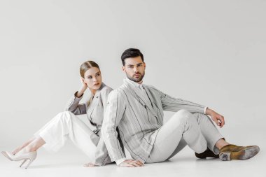 couple of attractive models in vintage clothes sitting on floor and leaning back to back on white clipart