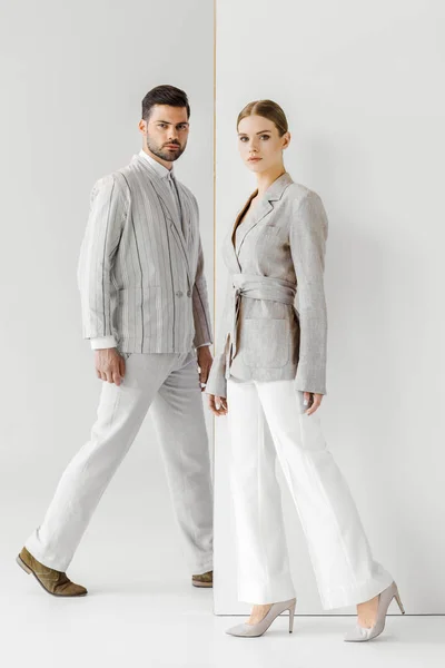 young male and female models in vintage clothes walking and looking at camera on white