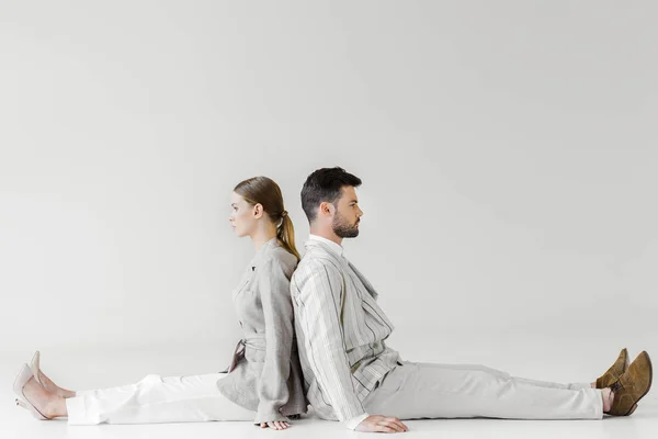 couple of models in vintage clothes sitting on floor and leaning back to back on white