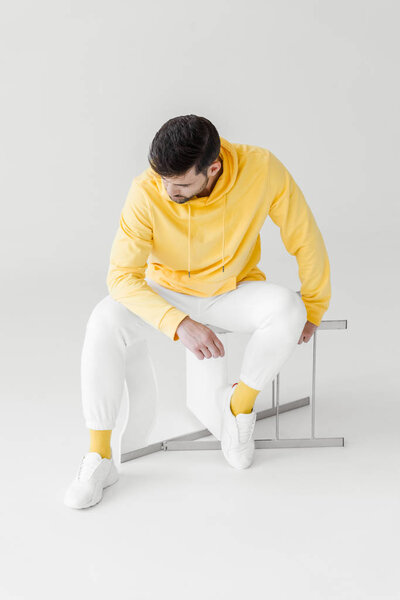 thoughtful young man in yellow hoodie sitting on flipped chair on white