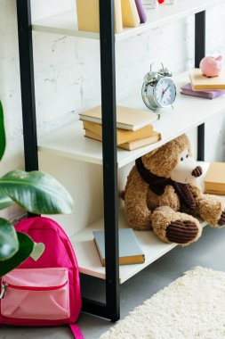 kitap, çalar saat ve oyuncak ayı raflarda ve halı üzerinde pembe okul çantası