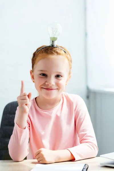 Vackra Skolflicka Med Lampa Huvudet Tittar Kameran Och Pekar Uppåt — Gratis stockfoto