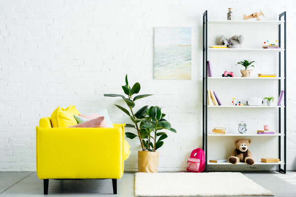 cozy interior with yellow couch and books with toys on shelves 