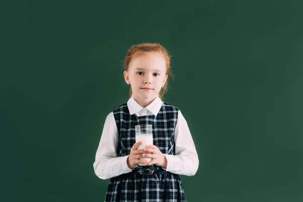 愛らしい小さな女子高生ミルクのガラスを保持して 黒板の近くに立っている間カメラで笑顔 — ストック写真