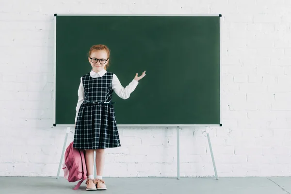 Adorável Colegial Com Mochila Mostrando Quadro Negro Branco Sorrindo Para — Fotografia de Stock