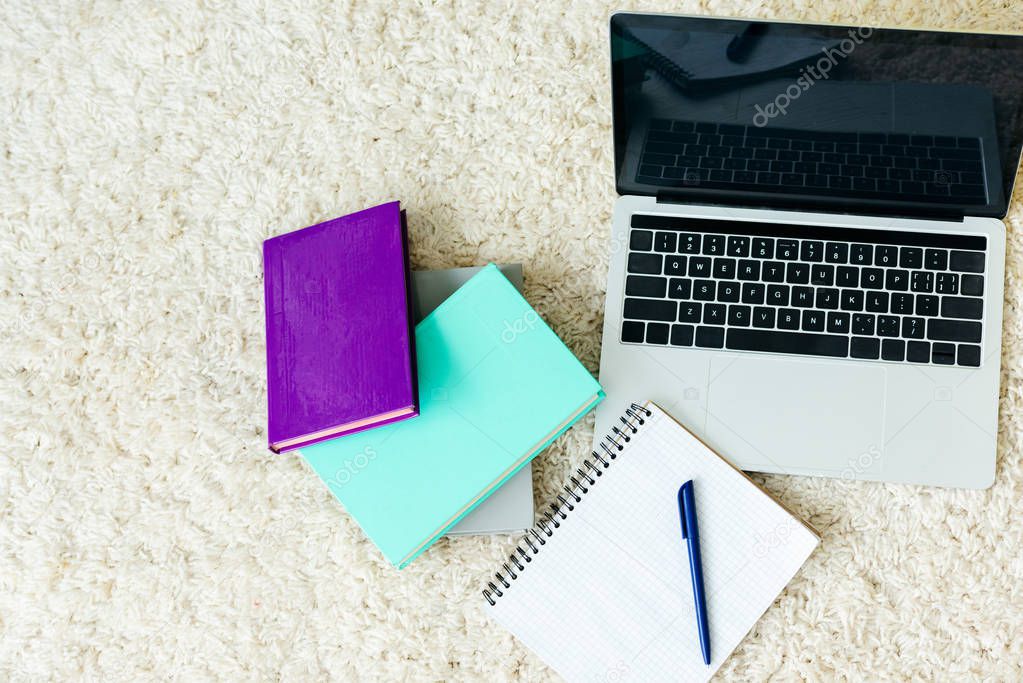 top view of books, notebook with pen and laptop with blank screen on carpet