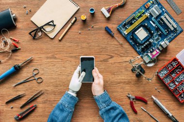 Araçlar tarafından çevrili masada smartphone kullanarak protez kollu elektronik mühendisinin resmini kırpılmış
