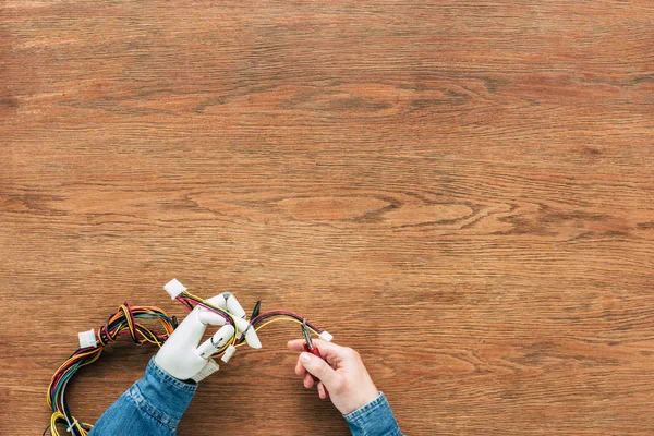 cropped image of man with prosthetic arm cutting wires by nippers at wooden table