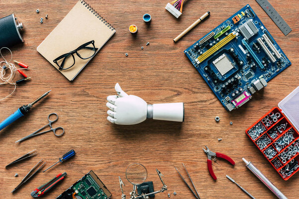 top view of prosthetic arm doing thumb up gesturing on table with tools