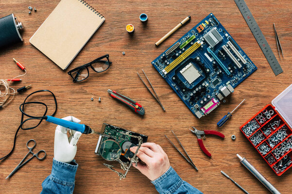 обрезанный образ человека с протезной рукой, восстанавливающей жесткий диск паяльником
