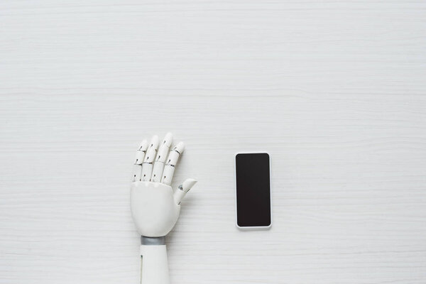 cropped image of prosthetic arm and smartphone with blank screen at wooden table 