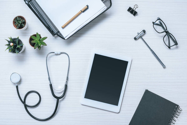 elevated view of doctor workplace with textbook, stethoscope, reflex hammer and digital tablet on table 