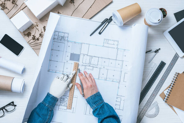 cropped image of male architect with prosthetic arm drawing on blueprint at table 