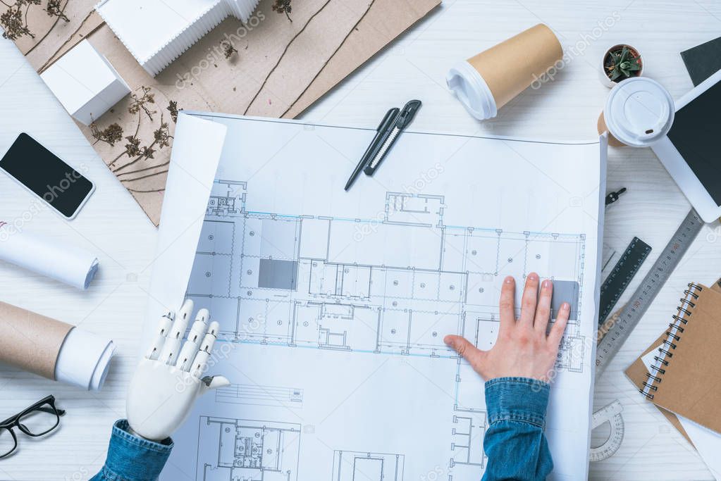partial view of male architect with prosthetic arm looking at blueprint 