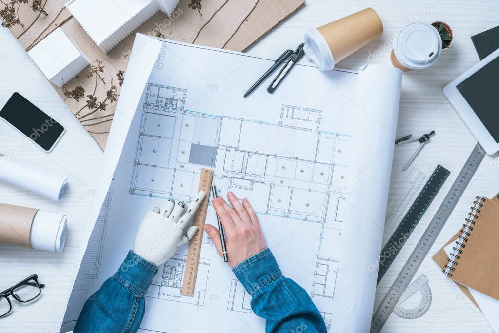 cropped image of male architect with prosthetic arm drawing on blueprint at table 