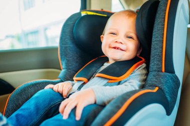 happy little baby sitting in child safety seat in car and looking at camera clipart