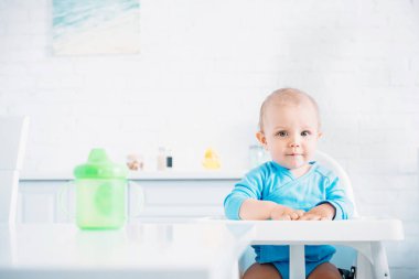 üzerinde high chair mutfak at ve kameraya bakarak otururken şirin bebek