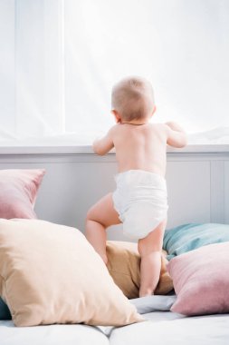 yatakta çok yastık ile ayakta ve pencereden bakarak mutlu küçük bebek