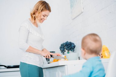 gülümseyen anne küçük çocuğunu o mama sandalyesi mutfak at oturan süre yemek hazırlama
