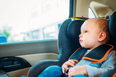 adorable little baby sitting in child safety seat in car and looking through window clipart