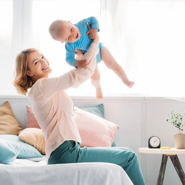 Lycklig Mamma Höjer Upp Skrattar Litet Barn Sittande Sängen Hemma — Stockfoto