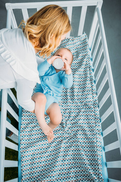 high angle view of mother putting her little child into crib at home