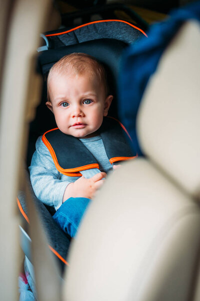 little baby sitting in child safety seat in car and looking at camera