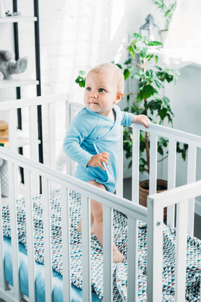 adorable little baby standing in crib and looking away