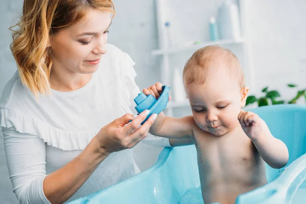 母が彼女の子供とおもちゃの船を自宅の浴槽で押しながらプレイ — ストック写真